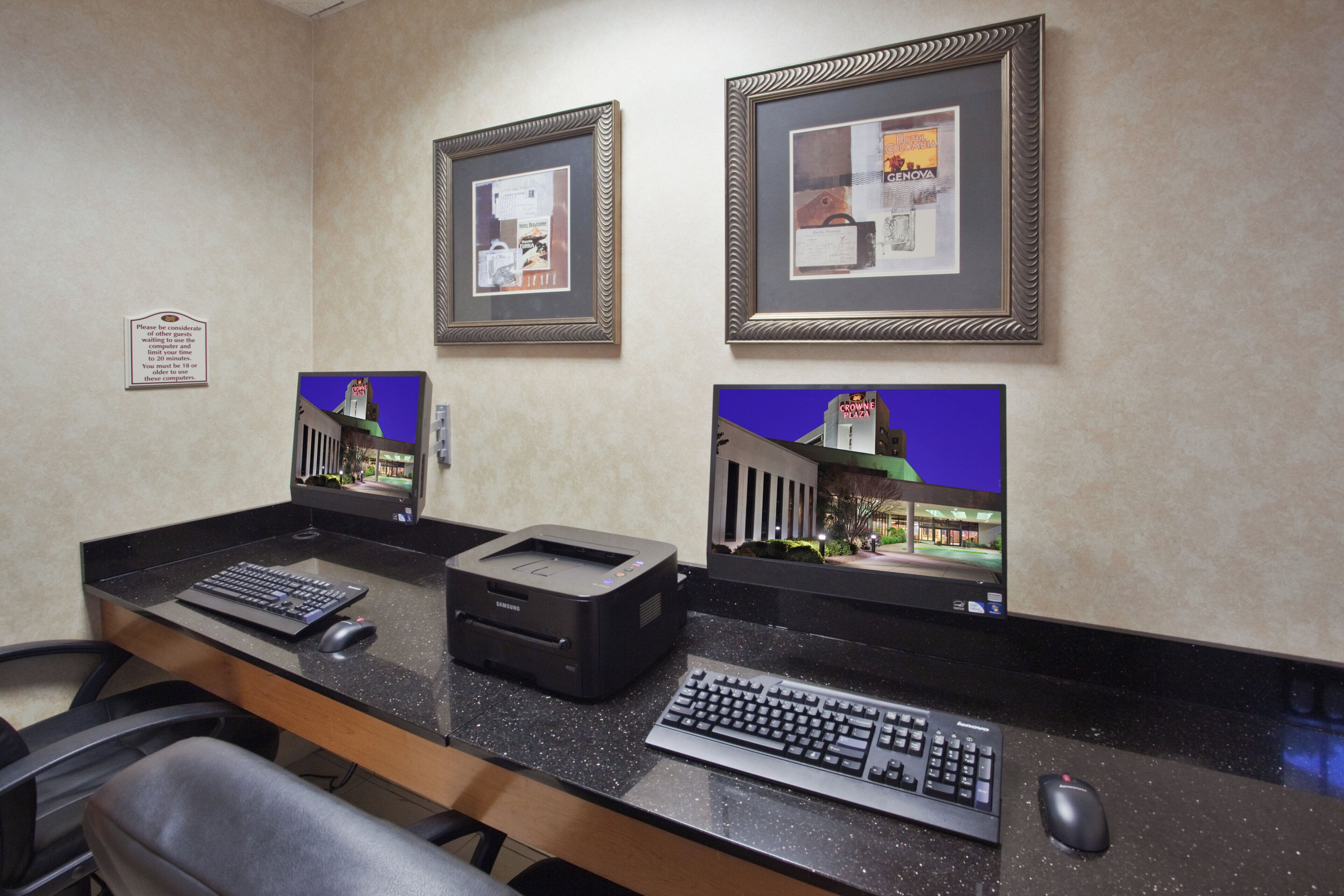 Un mostrador de recepción de hotel con dos cuadros enmarcados, una computadora e impresora.