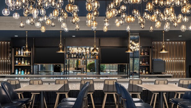 Uma área de bar moderna com diversos arranjos de assento e luminárias esféricas penduradas.