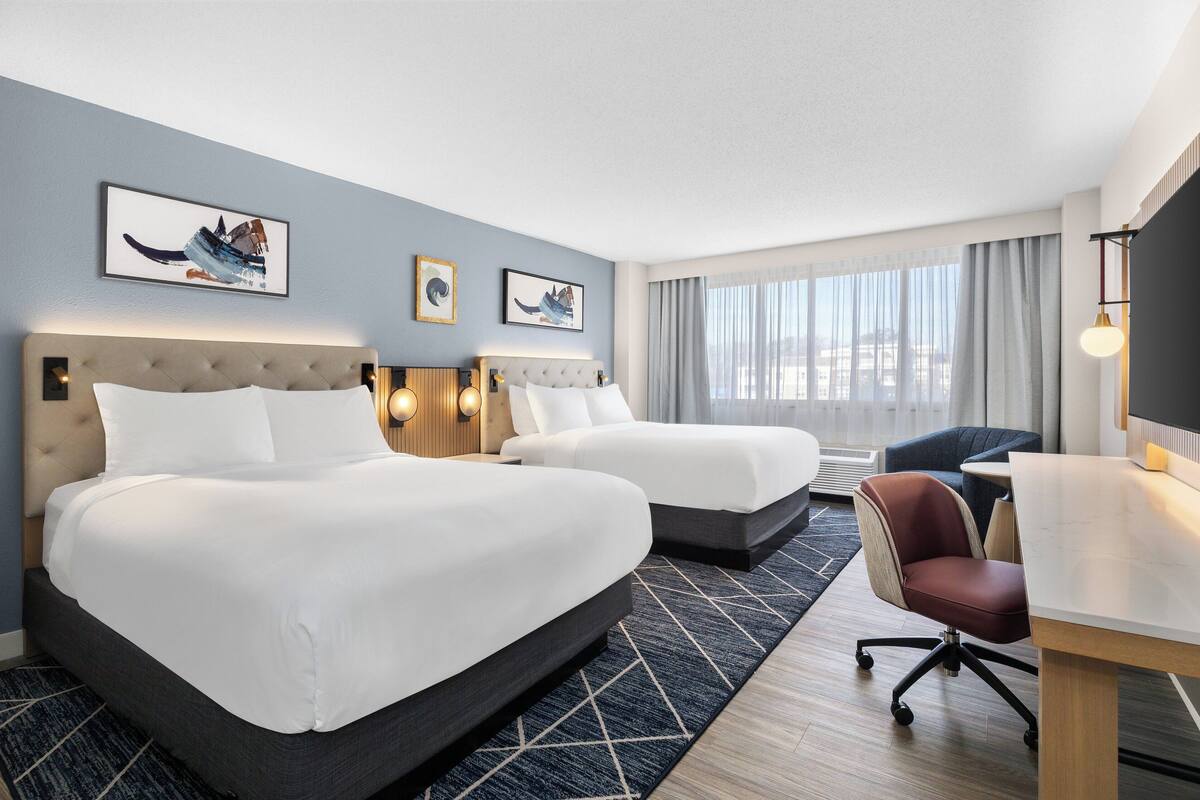 Ett hotellrum med två sängar, ett skrivbord, en stol och konstverk på väggarna.