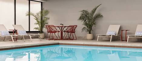 Zona de piscina con sillas de descanso y mesas, rodeada de plantas en macetas.