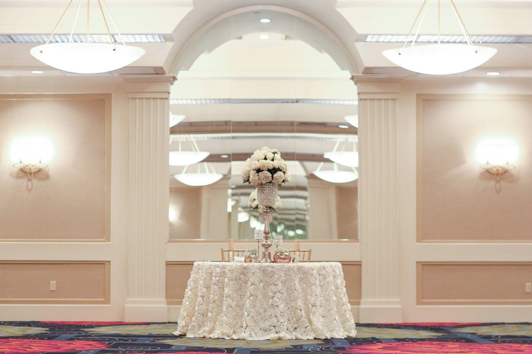 A hotel reception area with a reception desk, two wall-mounted light fixtures, and a large arched doorway.
