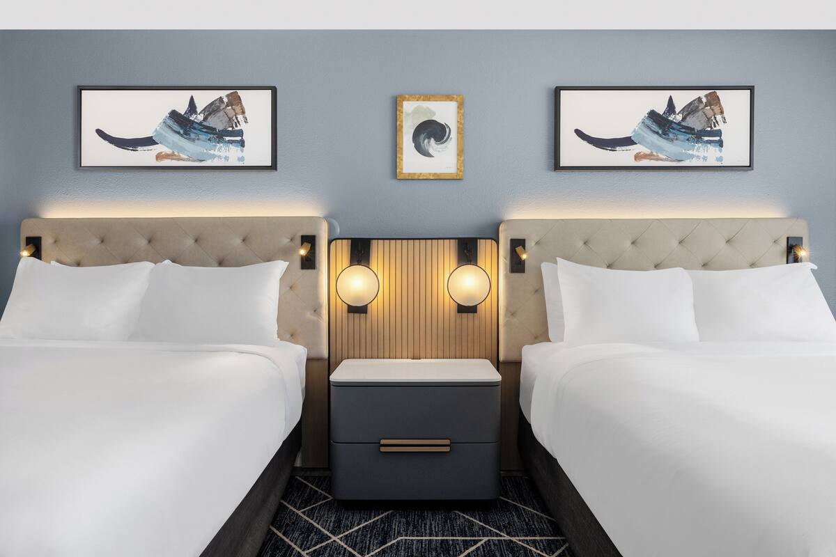 Ett hotellrum med två sängar, ett sängbord och konstverk som hänger på väggen.
