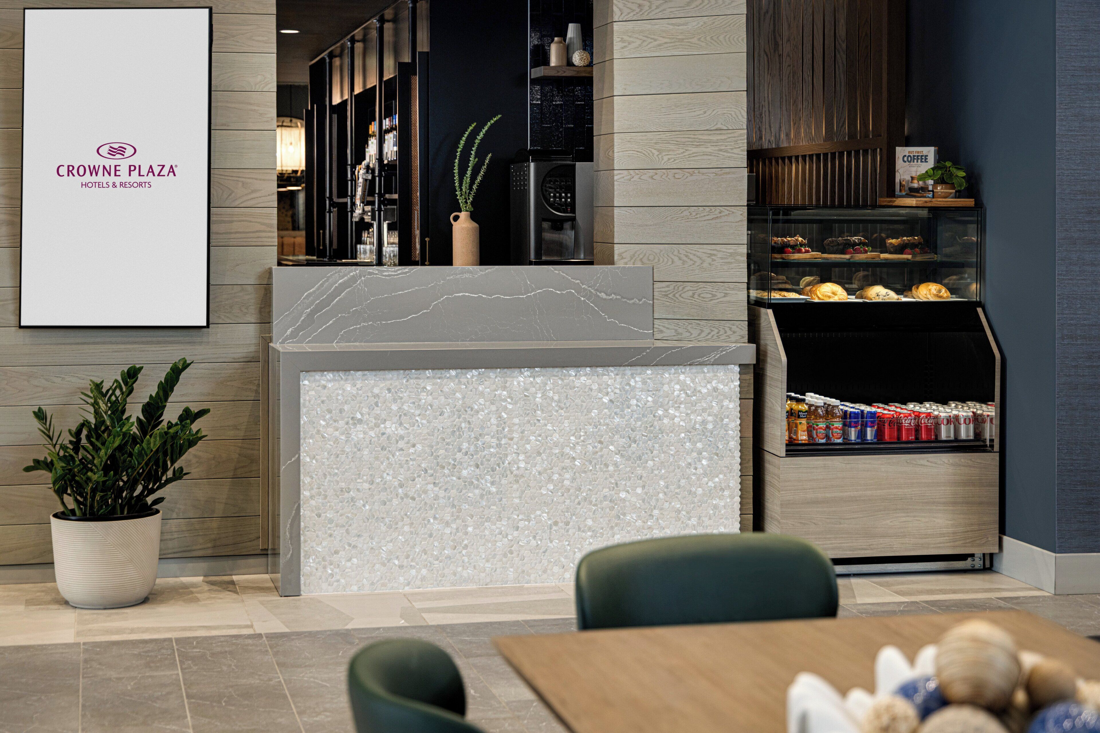 A modern hotel lobby with a reception desk, a coffee station, and a seating area.