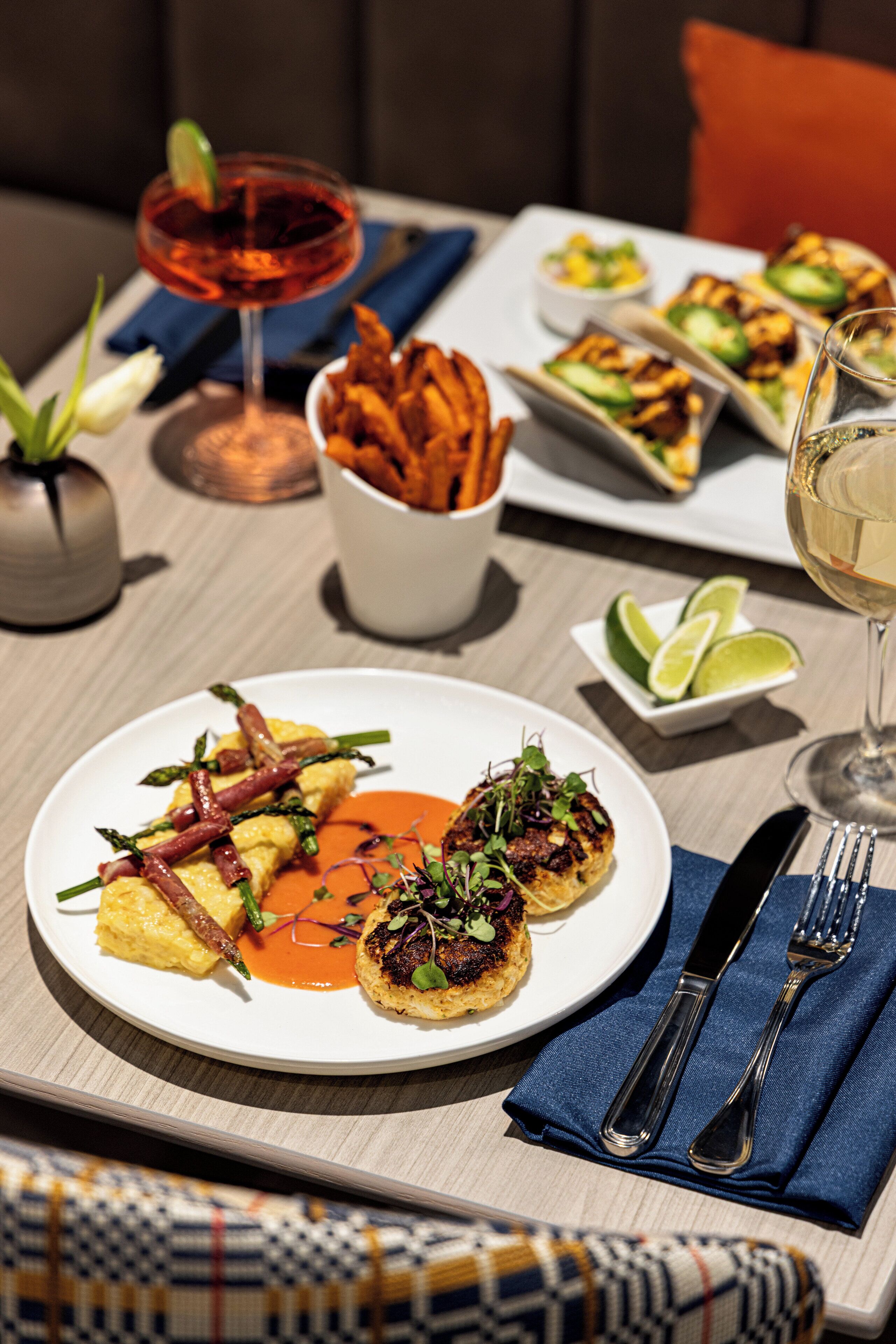 A dining table with plates of food, a glass of wine, and a bowl of chips.