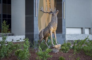 A deer sculpture in a landscaped garden area with a modern building in the background.