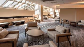 A spacious hotel lobby with a high ceiling, large windows, and a variety of seating options including sofas and armchairs.