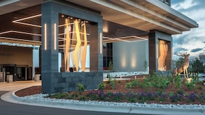 Una entrada de hotel moderna con una gran escultura de ciervo, un pasillo cubierto y un jardín ajardinado.