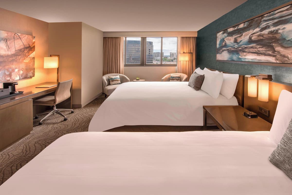 A hotel room with a large bed, a desk with a chair, a small table, and a window with curtains.