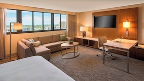 Habitación de hotel con cama, sofá, escritorio, silla, televisión y vistas a la ciudad.