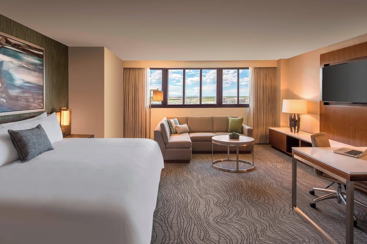 A hotel room with a large bed, a sofa, a small table, a desk, and a TV.