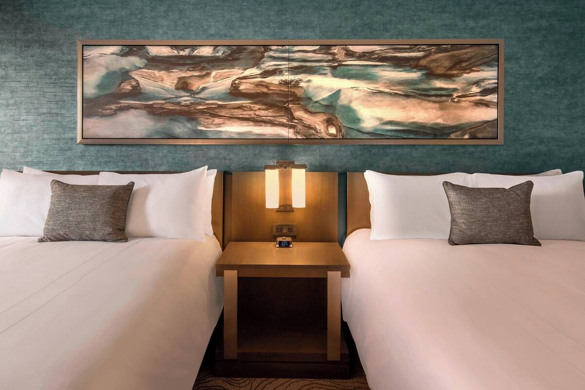 A hotel room with two beds, a nightstand with a lamp, and a large abstract painting above the beds.