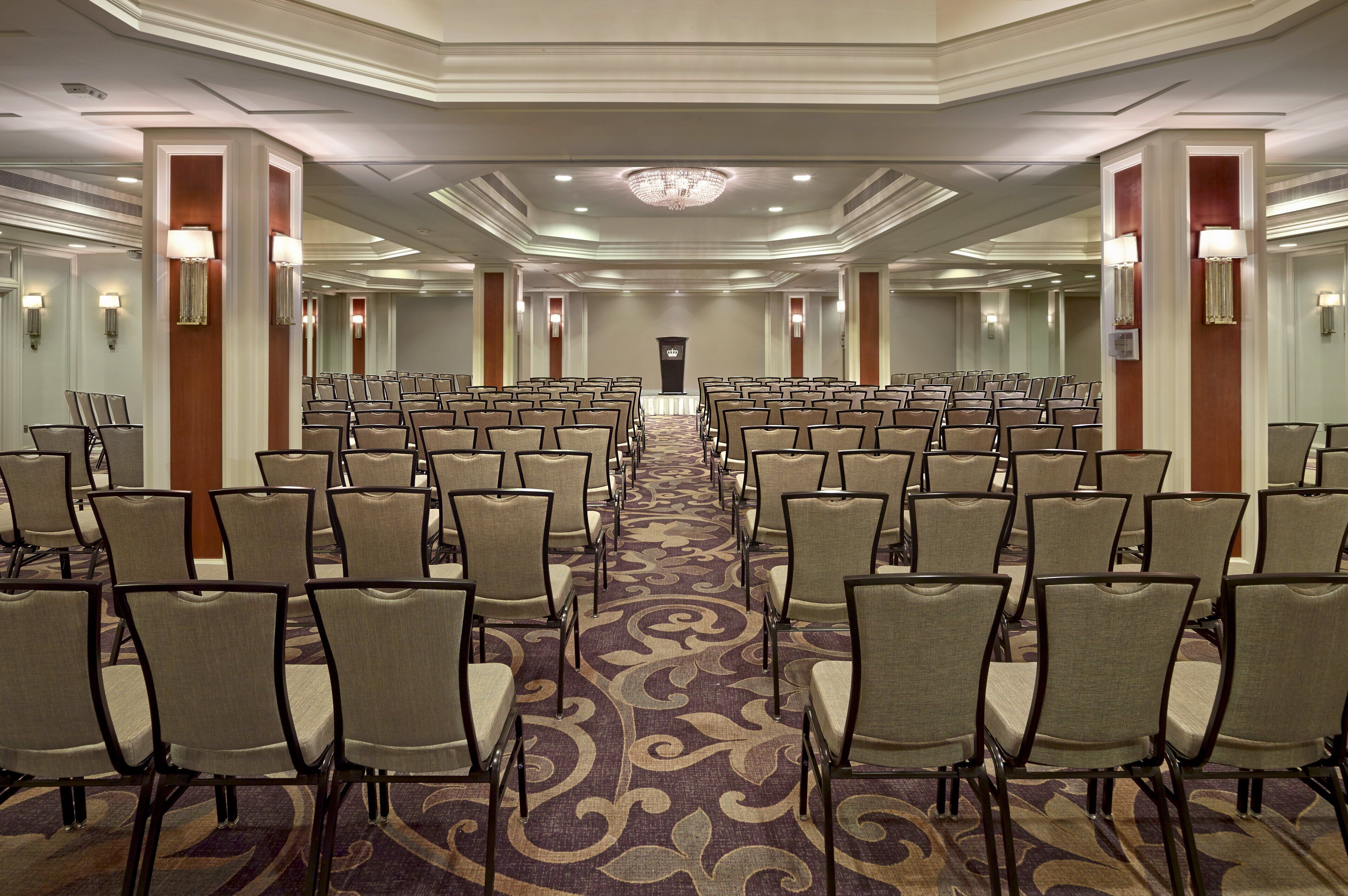 A conference room with rows of chairs, a patterned carpet, and wall sconces.