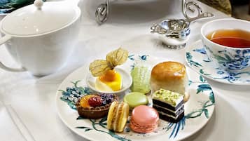 Un présentoir à trois niveaux, garni de diverses pâtisseries, et un service à thé disposés sur une table.
