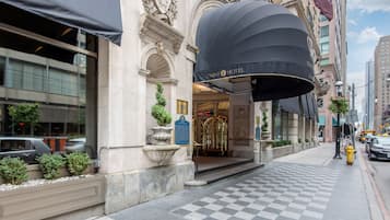 La entrada del Hotel Omni, con pavimento a cuadros, un toldo negro y una jardinera de piedra con plantas.