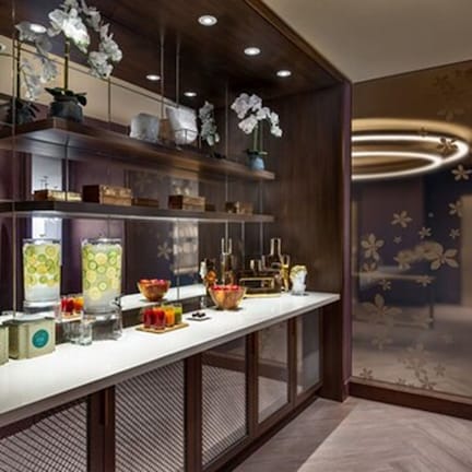 A modern hotel lobby with a long reception desk, shelves with decorative items, and a patterned wall.