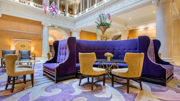 A lobby with a purple sofa, two patterned chairs, a table, and a decorative vase.