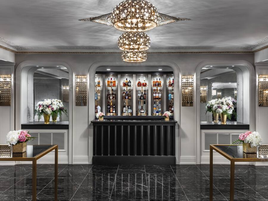 A luxurious lobby with a black reception desk, a chandelier, and a bar area with bottles and flowers.