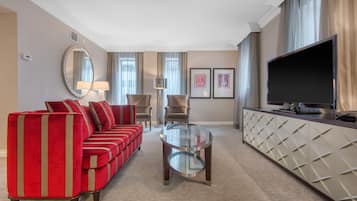 Una habitación de hotel con un sofá rojo, una mesa de centro de vidrio, un televisor y un minibar.