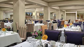 Un restaurante con varias mesas dispuestas para comer, cada una con mantel blanco, cubertería y cristalería.