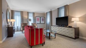 Habitación de hotel con sofá rojo, televisión, mesa de centro de vidrio y minibar.
