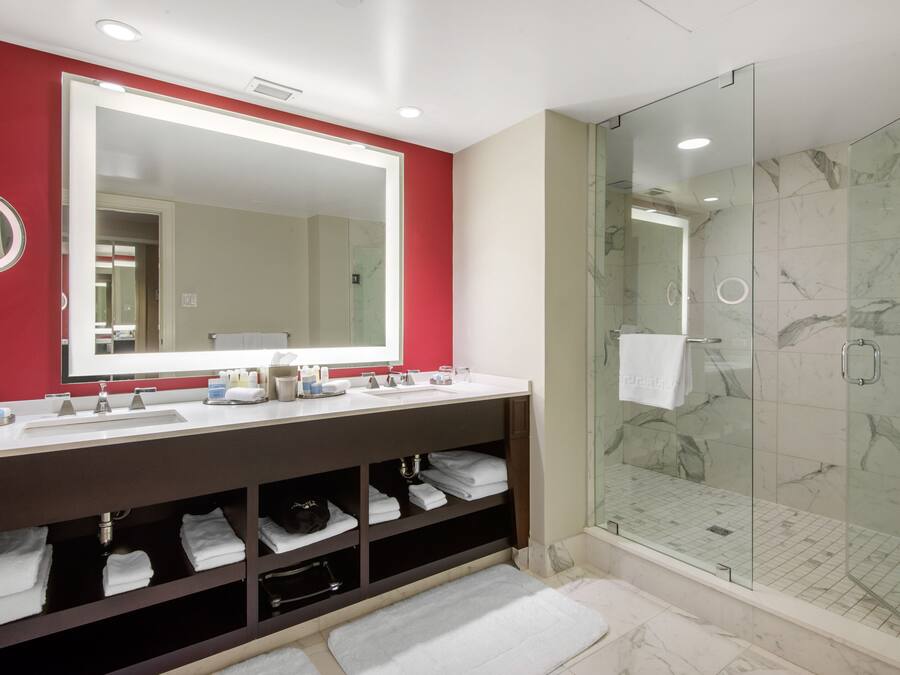 A modern bathroom with a large mirror, dual sinks, a glass shower enclosure, and neatly folded towels.