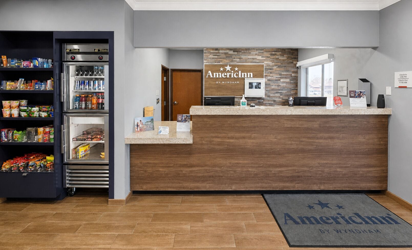 Un espace d’accueil avec un comptoir de réception en bois, un réfrigérateur rempli de boissons et un paillasson.