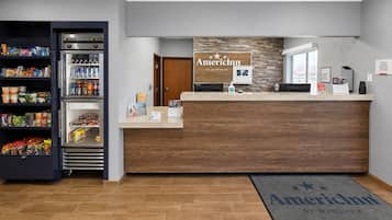 Un espace d’accueil avec un comptoir de réception en bois, un réfrigérateur rempli de boissons et un paillasson.