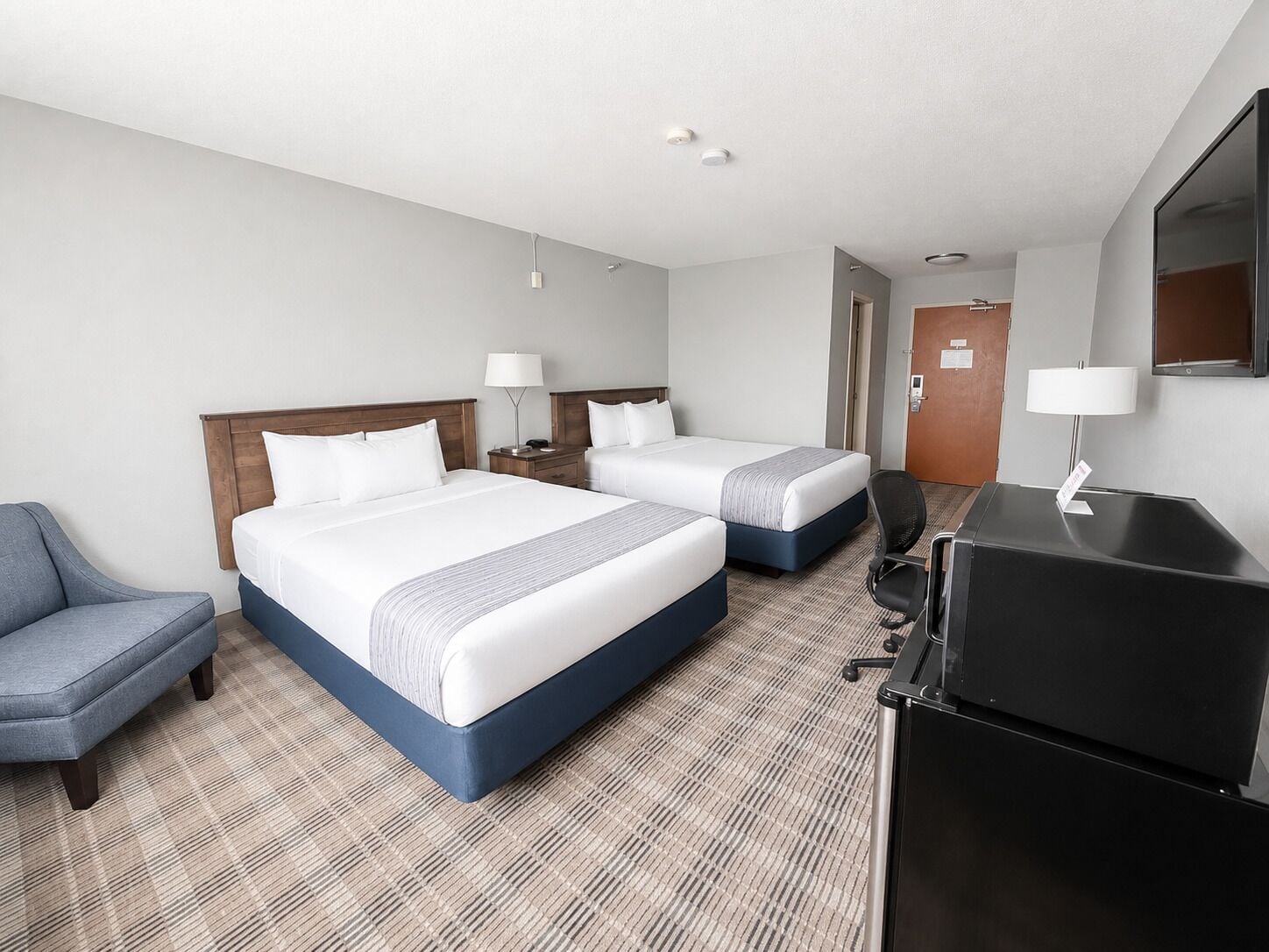 A hotel room with two beds, a desk, a chair, and a television.