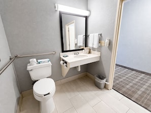 A modern bathroom with a toilet, sink, and mirror. - AmericInn by Wyndham Minot (Minot)