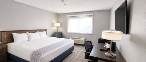 Een hotelkamer met een bed, bureau, stoel, lamp en een televisie aan de muur.