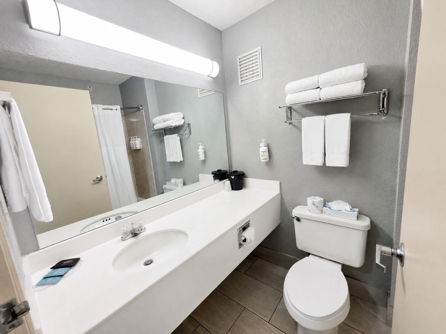 A modern bathroom with a large mirror, a double sink, a toilet, and towel racks.