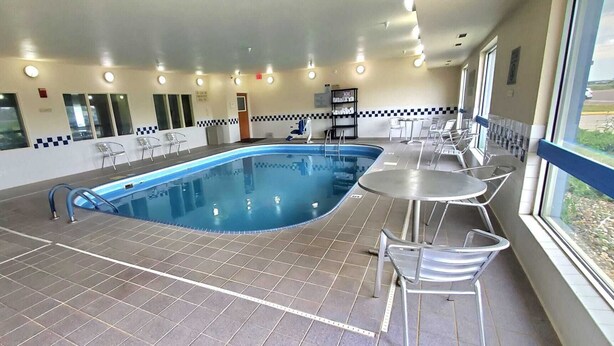 An indoor swimming pool with tiled flooring, a few lounge chairs, and a view of the outdoors through a window. - AmericInn by Wyndham Minot (Minot)