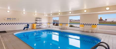 An indoor swimming pool with a clear view of the outside, a tiled floor, and a seating area with chairs.