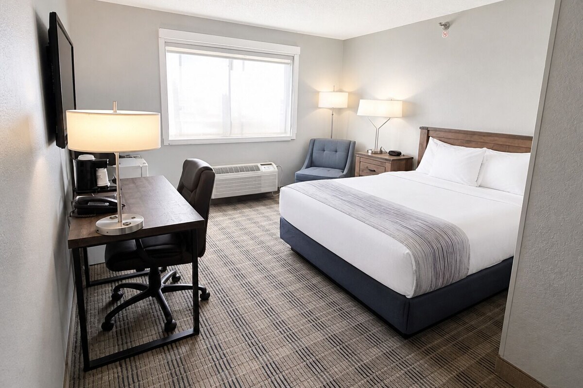 A hotel room with a bed, desk, chair, lamps, and a window.