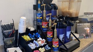 A coffee station with Torani syrup bottles, a coffee machine, and a beverage dispenser. - AmericInn by Wyndham Minot (Minot)