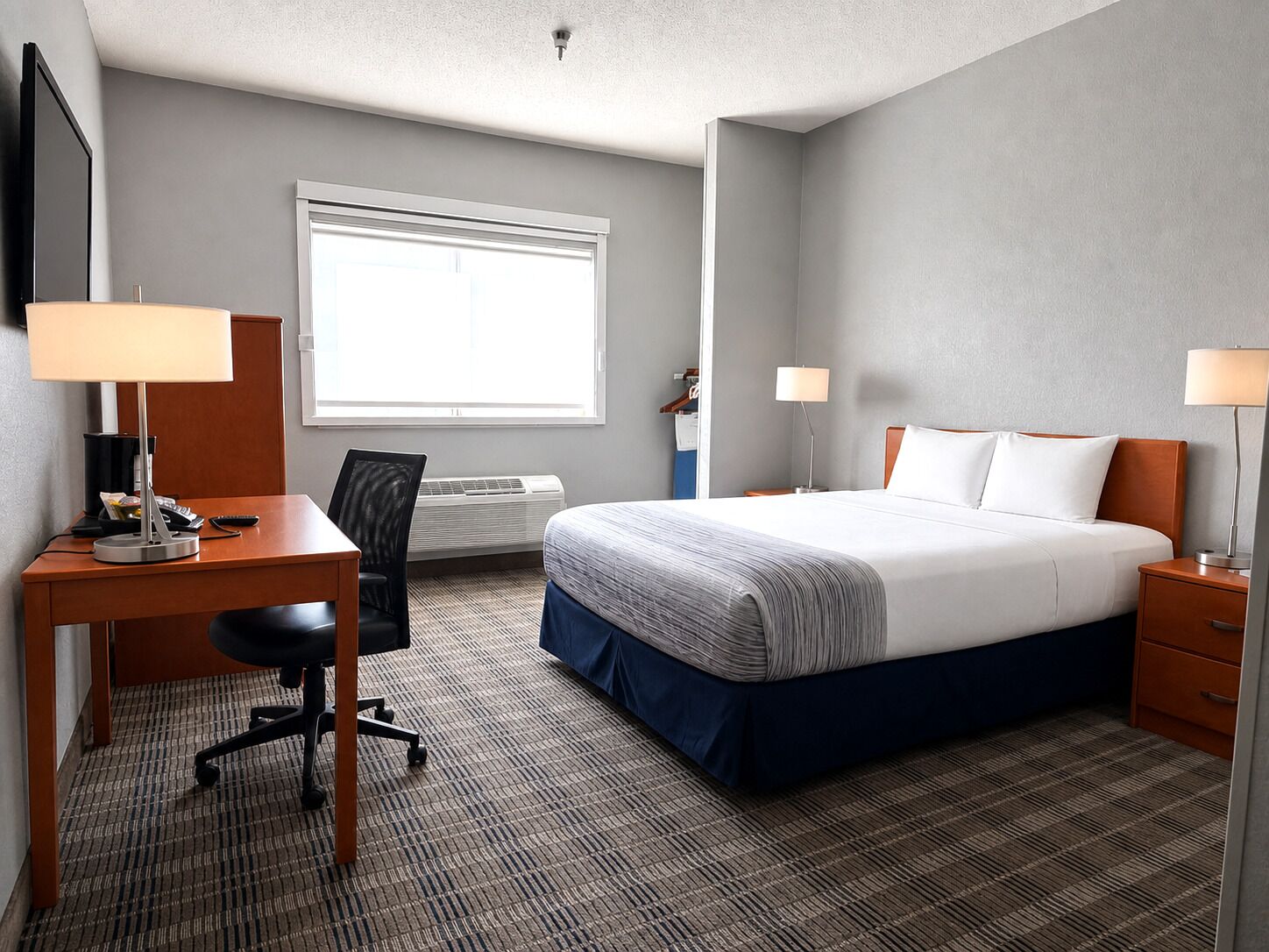 A hotel room with a bed, desk, chair, and a window.