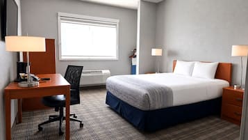 A hotel room with a bed, desk, chair, and a window.