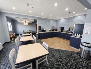 A hotel room with a kitchenette, a dining area with tables and chairs, and a patterned carpet.