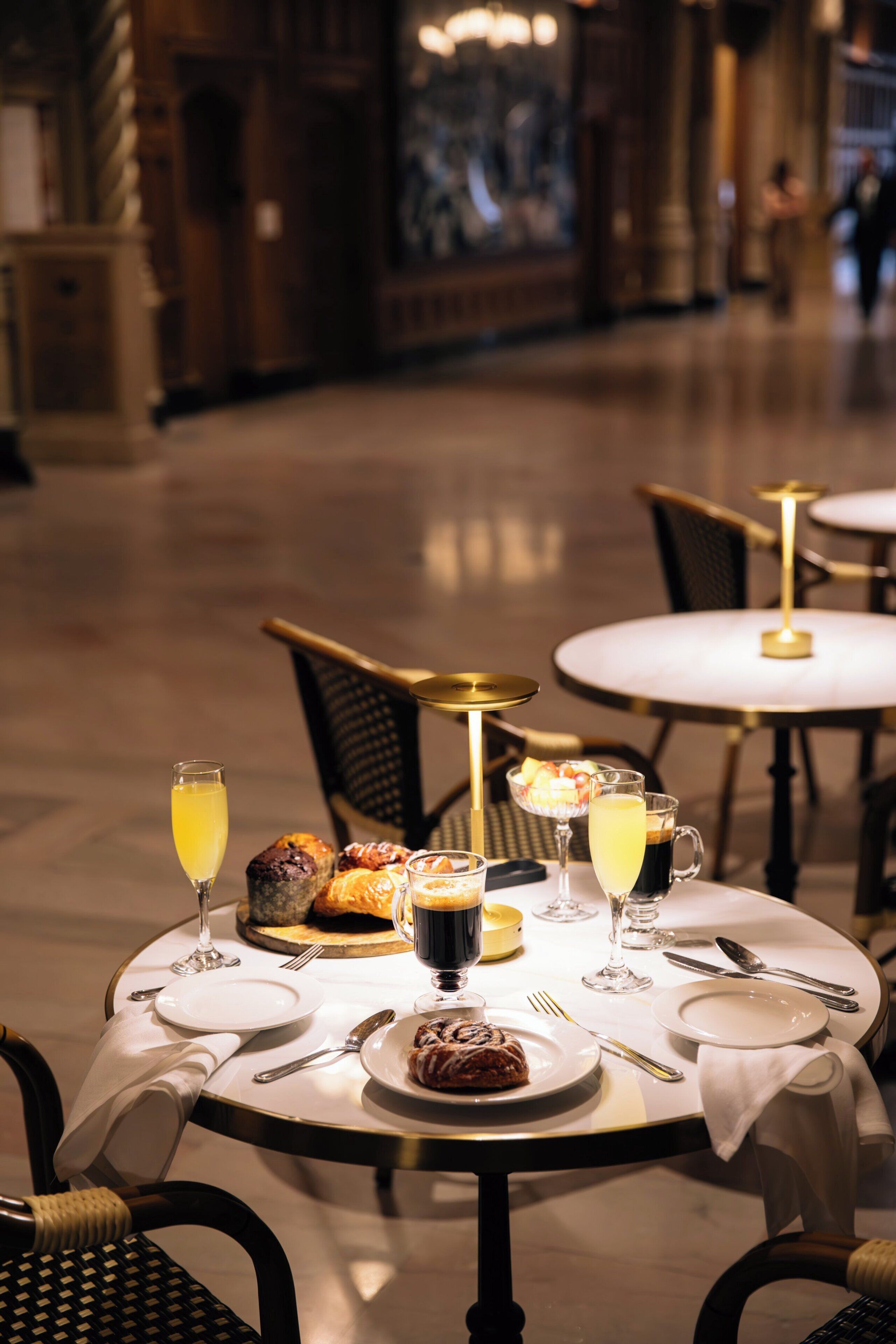 A dining area with round tables, chairs, and a variety of food and drinks.
