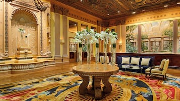 A grand lobby with ornate columns, a central round table with vases, and a blue sofa.
