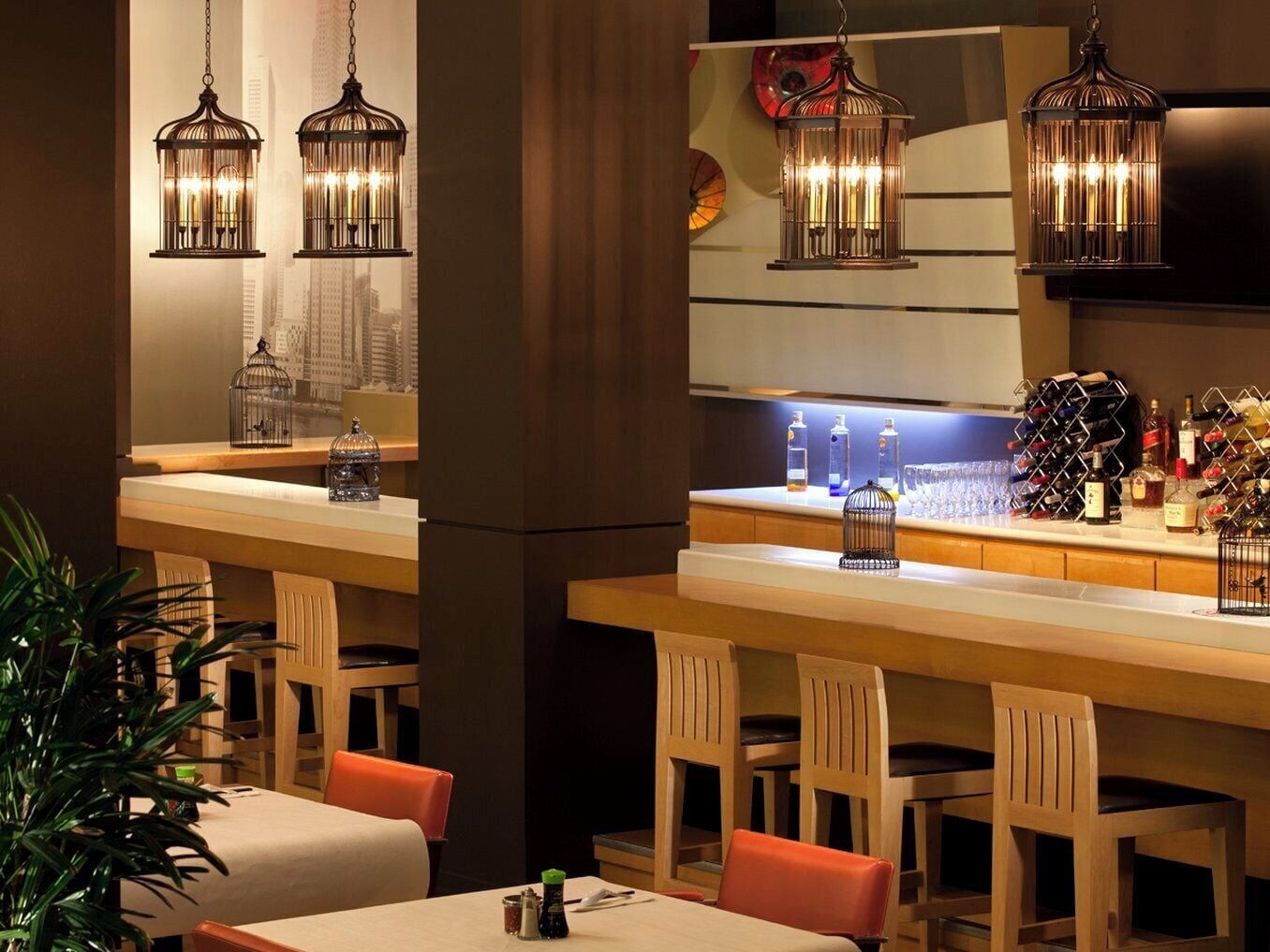 A bar area with hanging lanterns, a cityscape view, and a wine rack.
