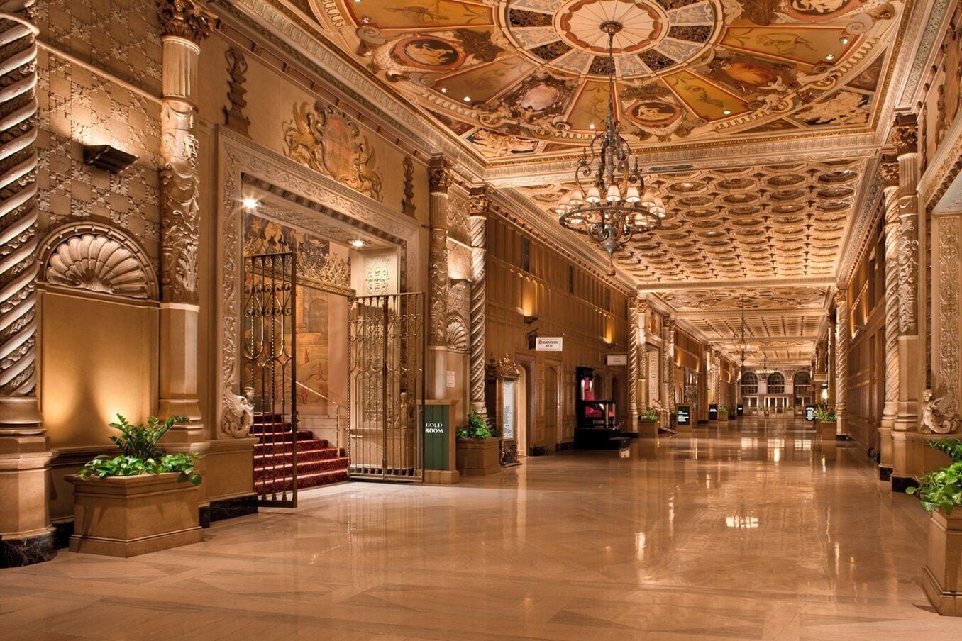 En storslået hotellobby med detaljerede søjler, en lysekrone og et skilt, der angiver et guldrum.