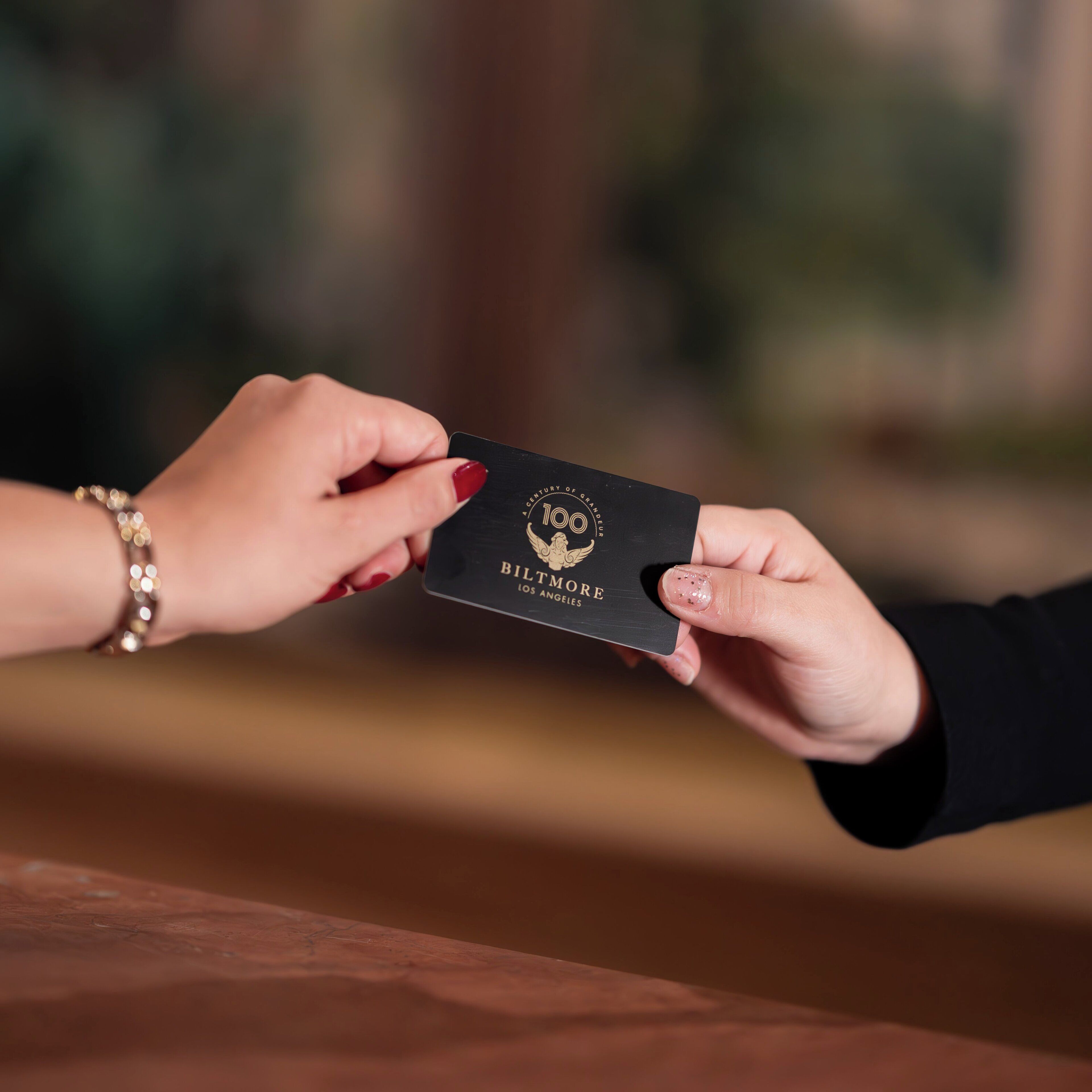 A hand holding a black card with gold text and a logo, another hand is reaching for it.