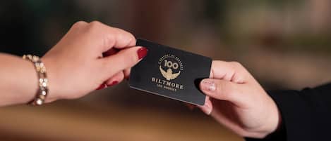 A hand holding a black card with gold text and a logo, another hand is reaching for it.