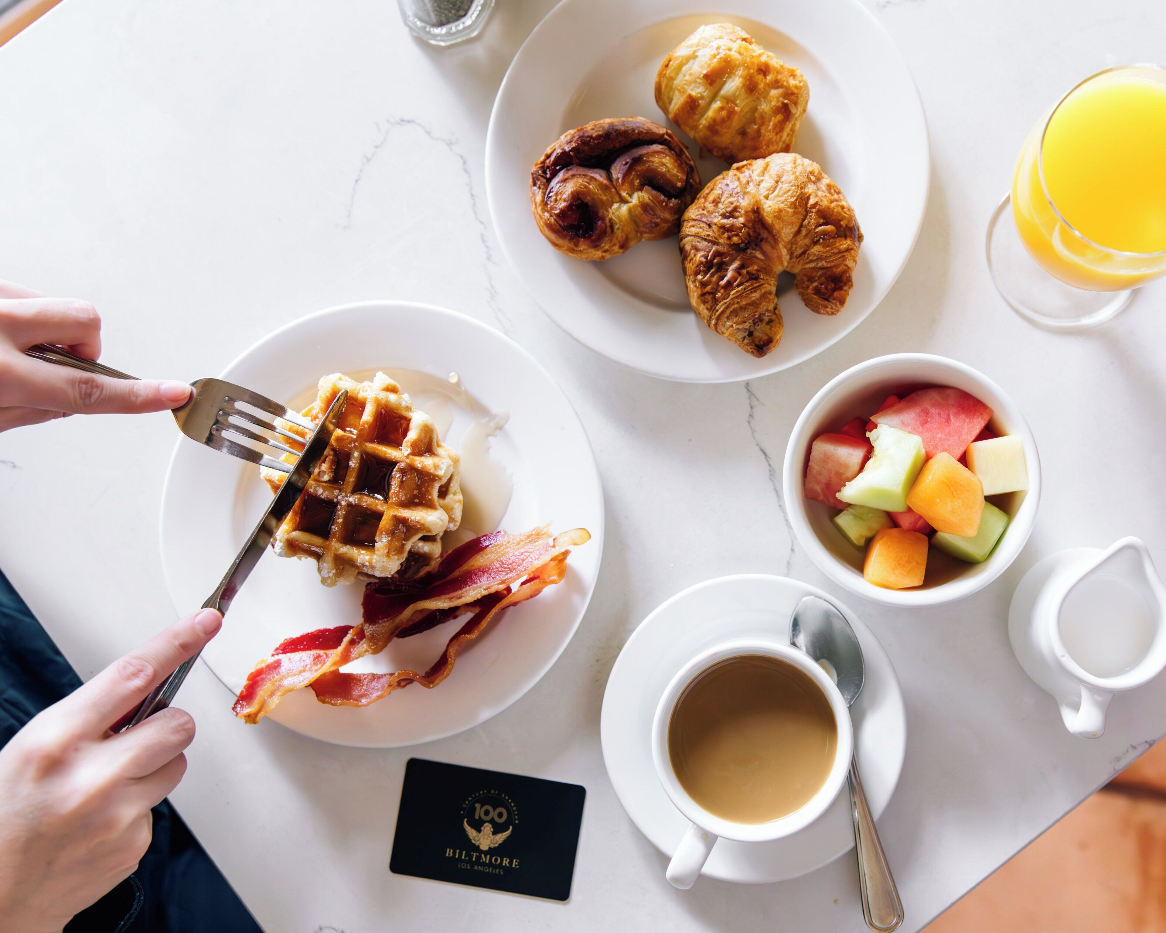 A breakfast setting with waffles, croissants, and a fruit bowl on a white table.