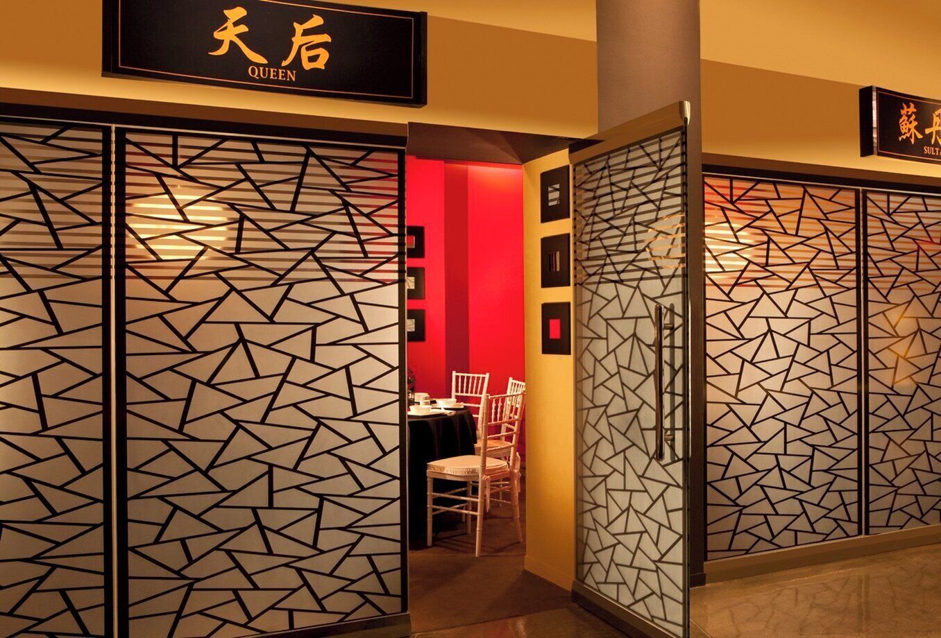 A hotel entrance with a geometric patterned door, a sign reading 'QUEEN,' and a glimpse of an interior dining area.
