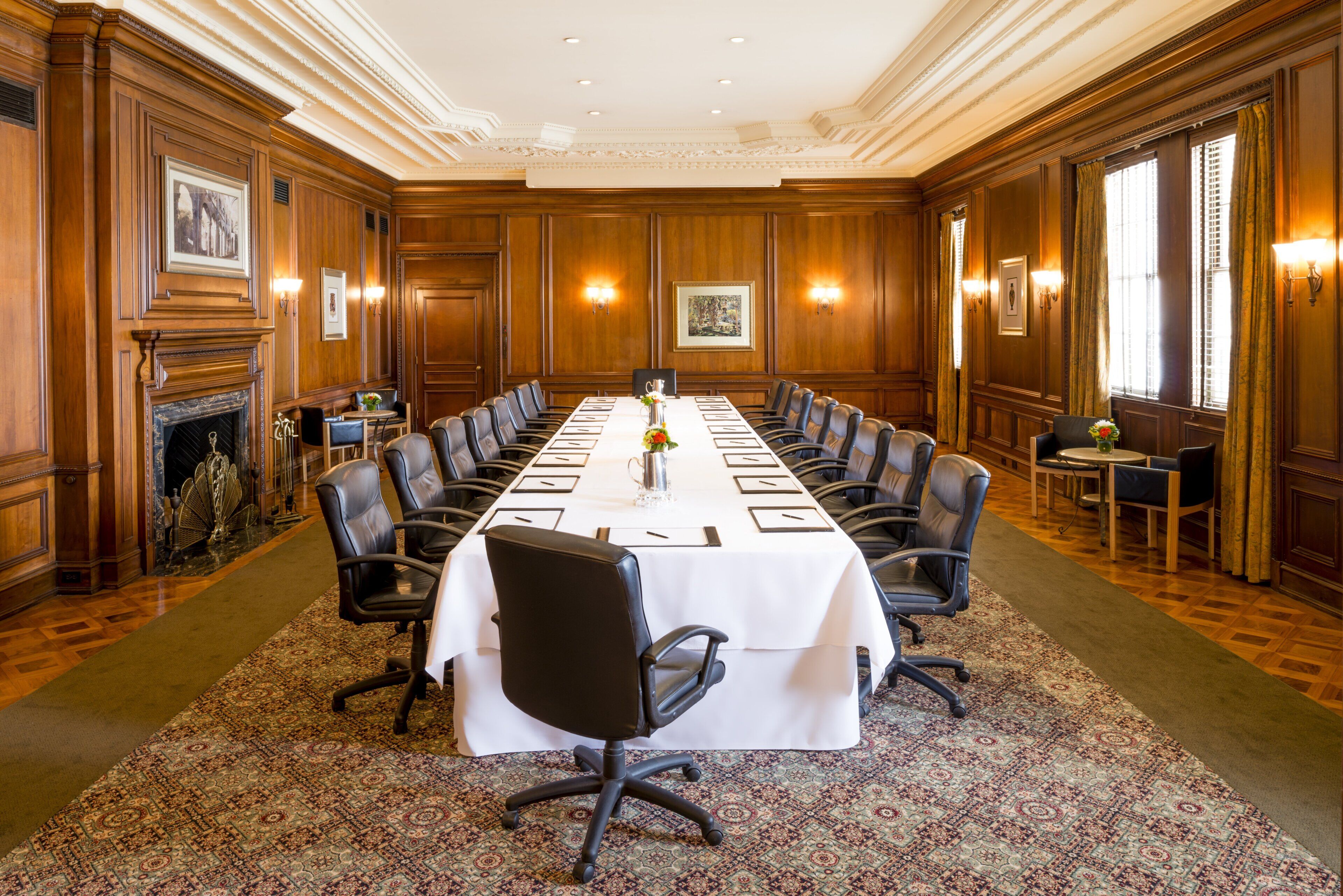 A conference room with a long table, chairs, a fireplace, and framed pictures on the walls.