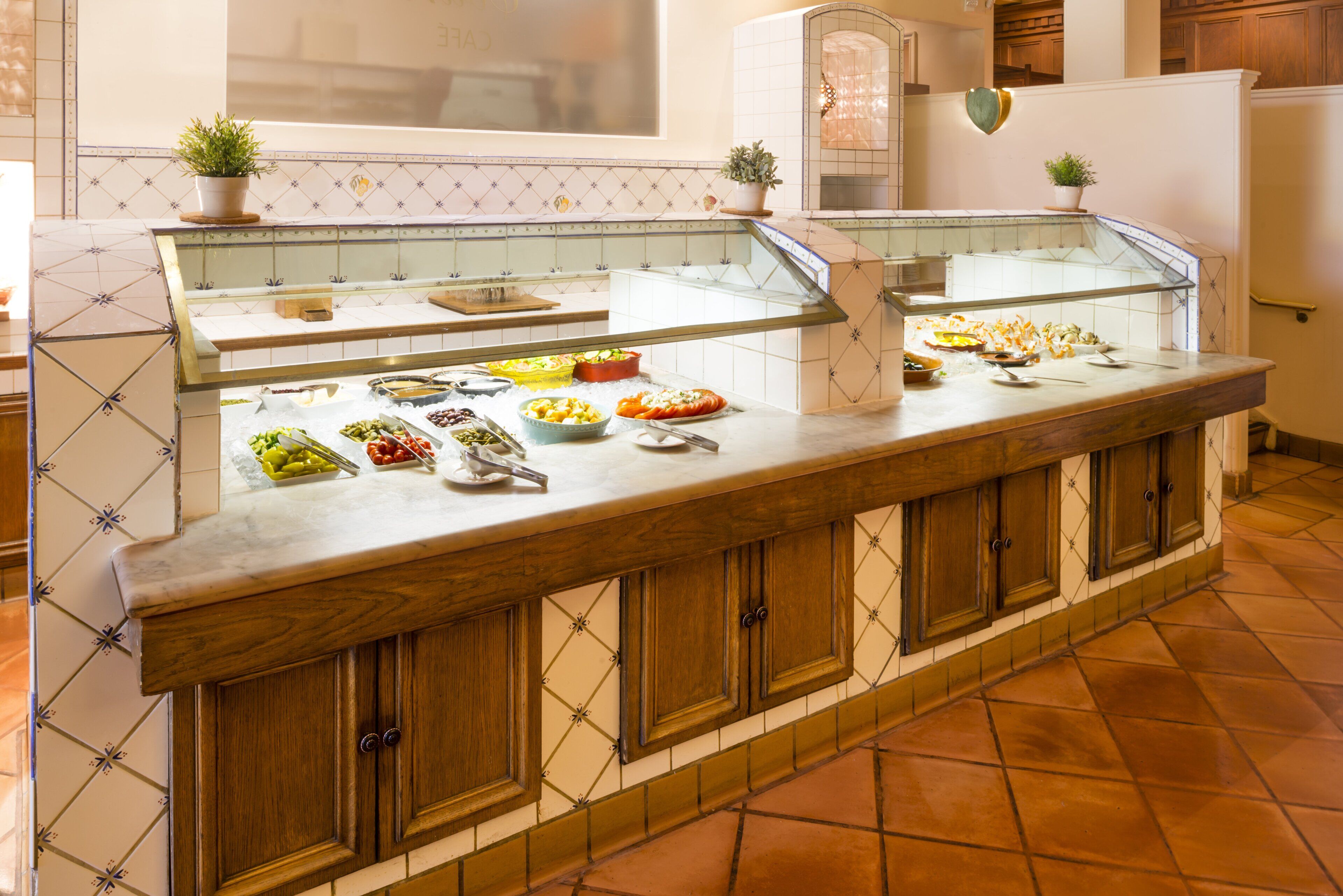 A buffet counter with various food items, a glass display case, wooden cabinets, and tiled flooring.