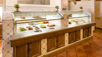 A buffet counter with various food items, a glass display case, wooden cabinets, and tiled flooring.