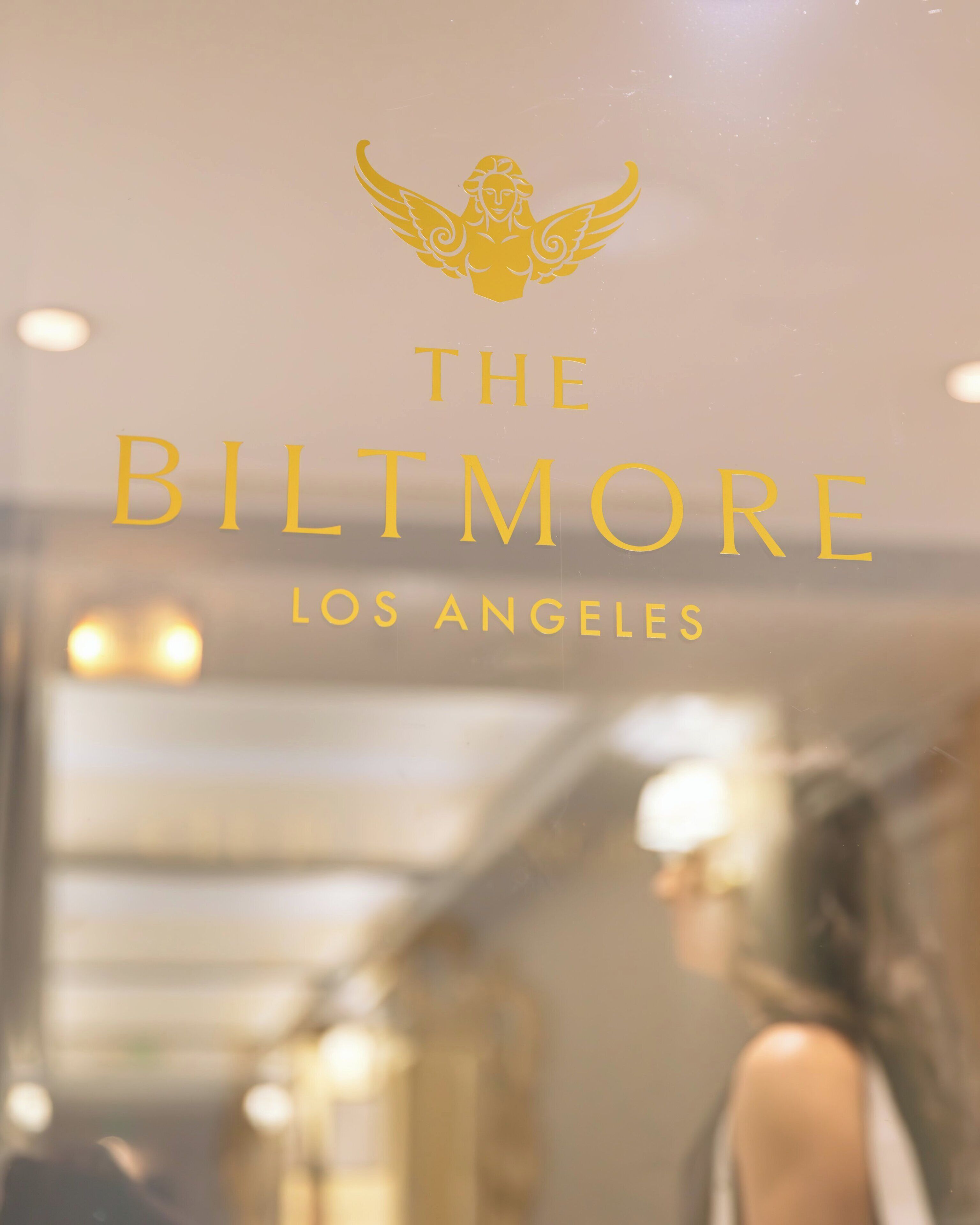 A blurred interior view of a hotel with a golden emblem and the text 'The Biltmore Los Angeles' prominently displayed.